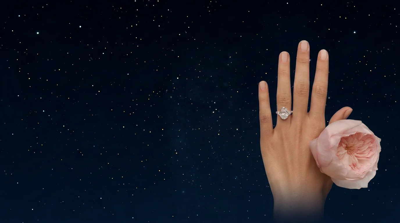 Hand wearing a three-stone oval diamond engagement ring, holding a pale pink garden rose against a deep navy starry sky